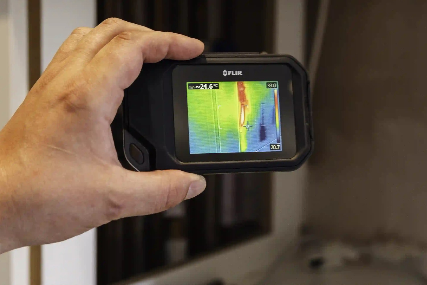 An ADI engineer holding a thermal imaging camera up to a wall, the screen showing the heat trail of a hidden hot pipe